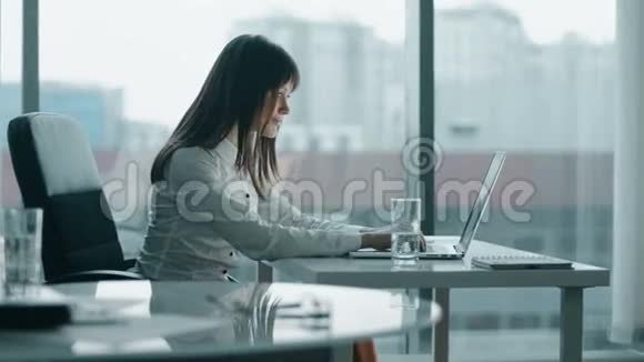 年轻的商业女性在现代办公室的笔记本电脑上工作她微笑着休息一下视频的预览图