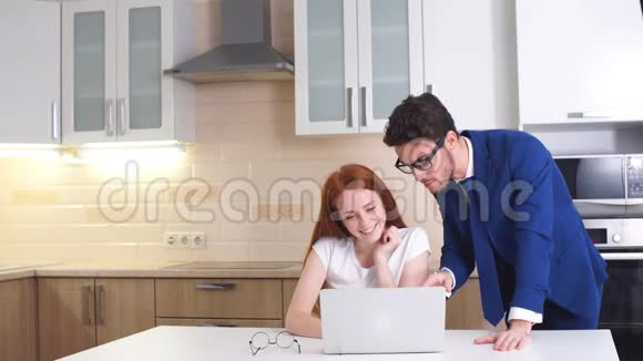 快乐的商务夫妇在厨房的家里看笔记本电脑视频的预览图