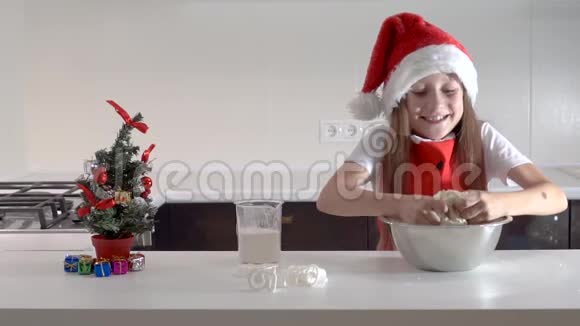 可爱的少女戴着圣诞老人的帽子和红色的圣诞围裙用自己的手从面团里切出饼干视频的预览图