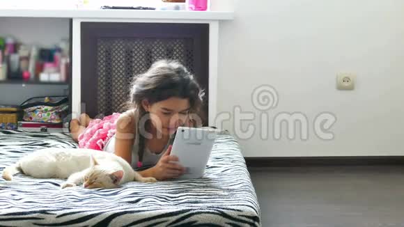 女孩玩平板电脑网络游戏坐在猫旁边视频的预览图