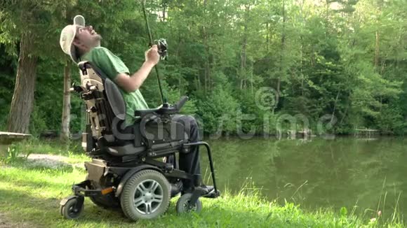 阳光明媚的一天坐在电动轮椅上的快乐男人在纳图美丽的池塘边钓鱼视频的预览图