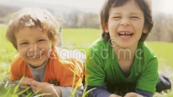 快乐的孩子们微笑着特写肖像在草地上躺着的两个哥哥小孩一边笑一边玩视频的预览图