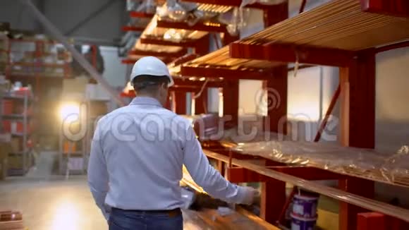 跟踪员工男性仓库工人工程师戴安全帽工作的镜头穿过物流中心视频的预览图