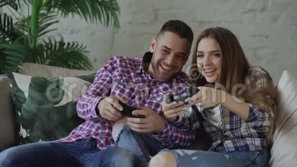 年轻快乐可爱的一对夫妇玩游戏游戏游戏在家的客厅里坐在沙发上玩得很开心视频的预览图