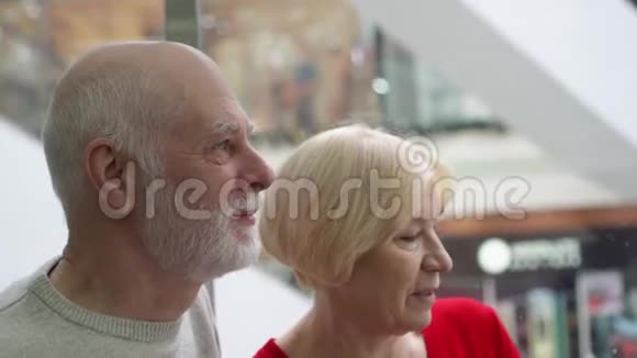 浅的景深把注意力集中在高级男人身上快乐的老夫妇坐电梯上现代商场视频的预览图
