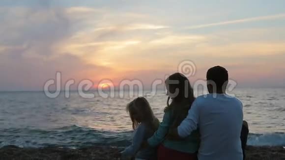 幸福的一家人坐在海边的夕阳下视频的预览图