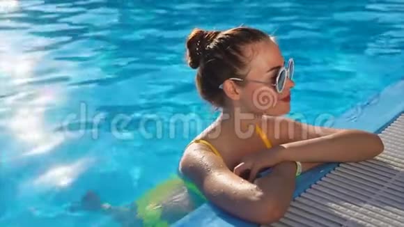 一位身穿泳衣的年轻女子正在游泳池里喝着清凉的水一个炎热的夏日视频的预览图