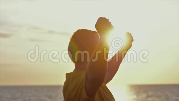 成功的年轻人正在海滩上美丽的日落时分慢腾腾地跳着舞蹈举起双手视频的预览图