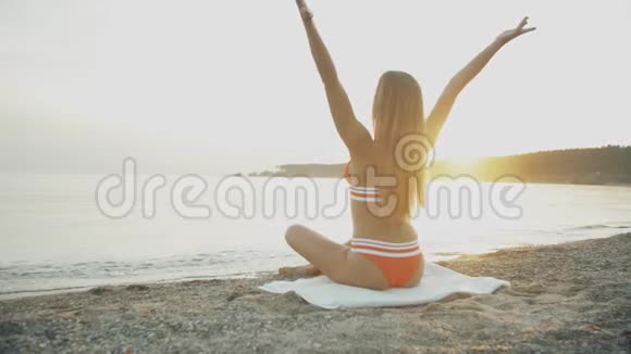 那个年轻女孩的剪影在日落时缓慢地摆弄她的头发晚上冥想女人在海边练习瑜伽视频的预览图