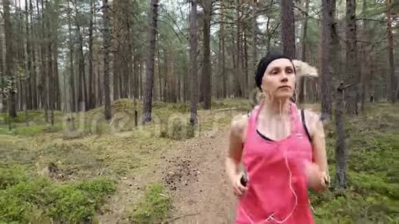 女人在森林小径上奔跑听着智能手机里的音乐视频的预览图