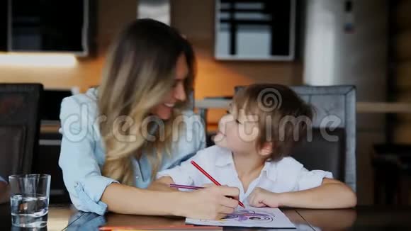 美丽的妈妈帮助她的儿子用彩色铅笔画图像帮助培养孩子想象力视频的预览图
