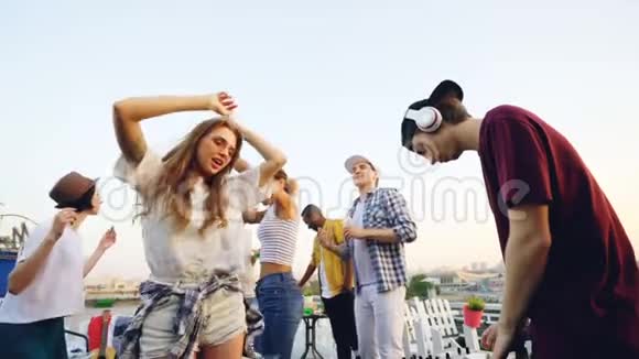 戴着无线耳机的美女戴着墨镜在屋顶和朋友跳舞时动作缓慢视频的预览图
