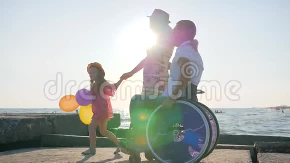 幸福的家庭残疾人在轮椅上与怀孕的妻子散步孩子拿着气球和跳跃与妻子无效视频的预览图
