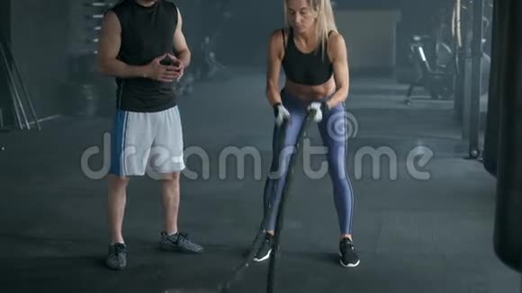 漂亮的健身女孩和教练正在做训练使用交叉绳索在健身房锻炼4K慢动作视频的预览图