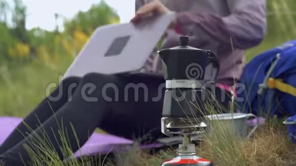 在山里露营一个女孩正在用间歇泉咖啡机准备咖啡一个女人为笔记本电脑远程工作视频的预览图