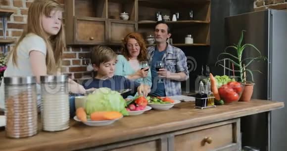 快乐的家庭在厨房父母看着孩子们一起烹饪食物一起切碎蔬菜视频的预览图