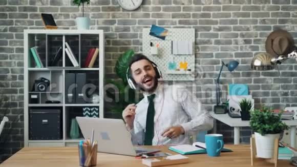 工作中听音乐唱歌跳舞的快乐男人用耳机视频的预览图