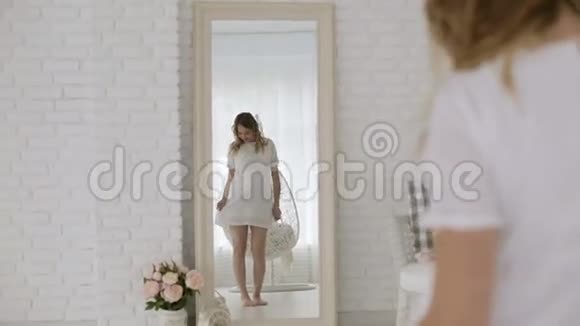 年轻的孕妇穿着白色连衣裙在镜子前跳舞视频的预览图