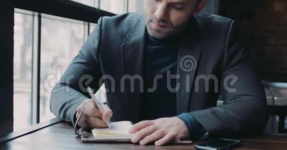 漂亮的男人穿着一套正式的黑色西装在文件上贴上签名然后朝相机看办公室视频的预览图