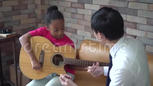 年轻的亚洲男老师给非裔美国女孩上吉他课教她弹吉他视频的预览图