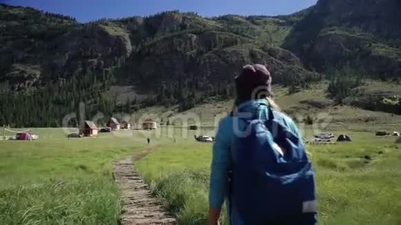 徒步旅行旅行者女孩带着背包和帽子走在山上的一座桥上露营在远处冒险视频的预览图