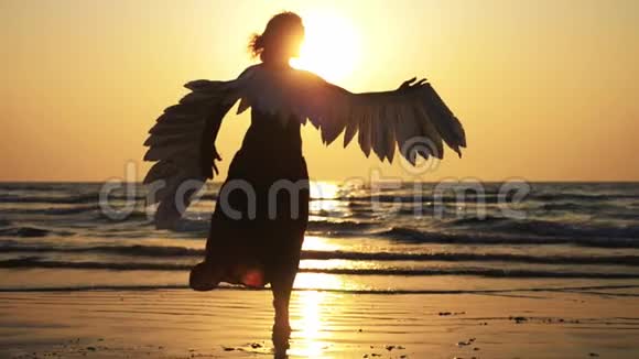 年轻女孩的剪影她带着翅膀在日落时慢动作地跳舞视频的预览图