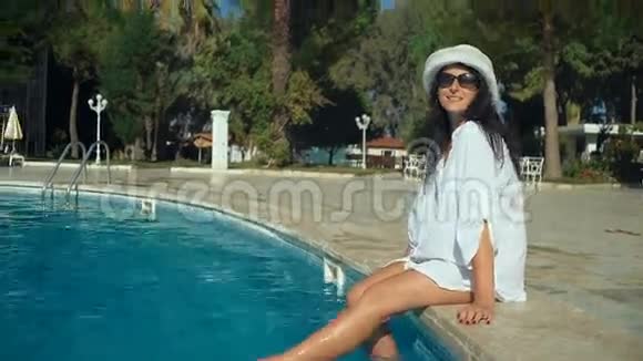 瘦小的年轻女人戴着帽子坐在游泳池的边缘长腿视频的预览图