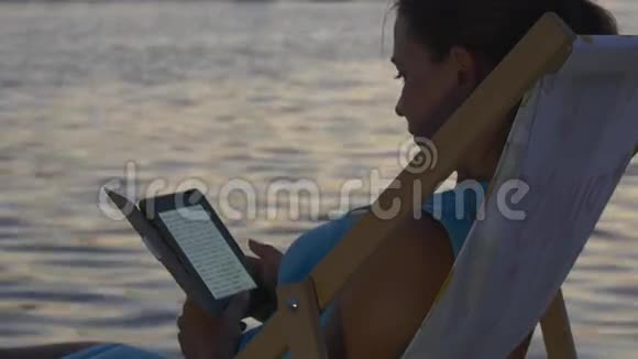 女人在夕阳下看一本电子书就在耀眼的水面上视频的预览图