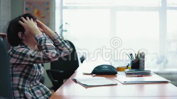 年轻的黑发女人坐在一张桌子前惊慌失措头痛视频的预览图