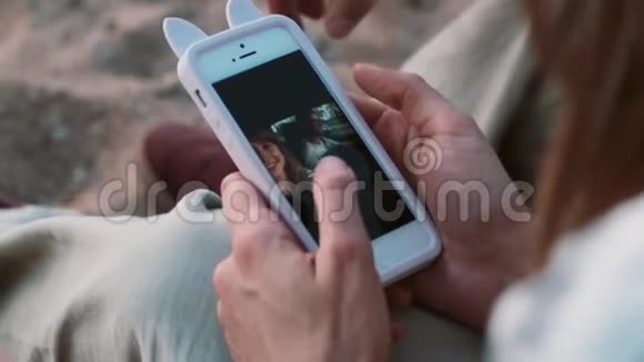 这对年轻夫妇坐在海滩上沙滩上在智能手机上看照片使用触摸屏视频的预览图