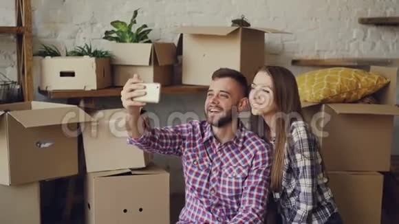 幸福的年轻夫妇在搬迁后用智能手机打视频电话他们在问候朋友展示新房子视频的预览图