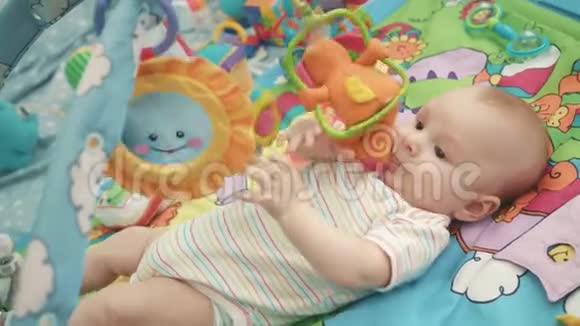 婴儿在五颜六色的垫子上玩耍可爱的小男孩玩玩具视频的预览图