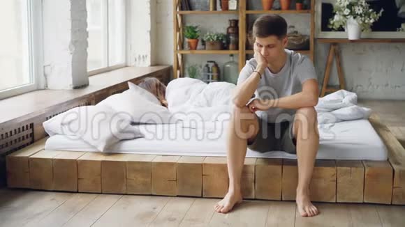 不高兴的丈夫坐在床上和妻子打架摸着他的脸一边叹息而他的妻子躺在床上视频的预览图