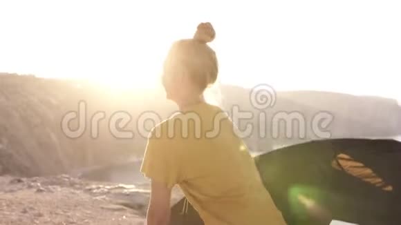 身着黄色T恤的女露营者的后侧场景展开双手迎接朝阳站在山上视频的预览图