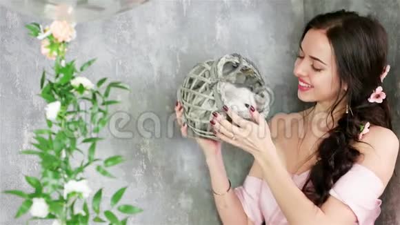 微笑的女士摆着相机手里拿着柳条灰色篮子里可爱的白兔春季拍照视频的预览图