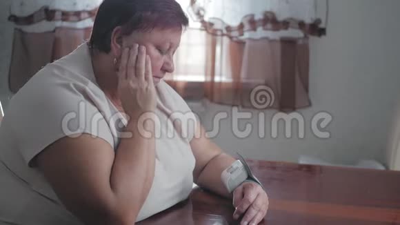 成熟的肥胖妇女坐在桌旁用数字血压计测量压力高级女性负责照顾视频的预览图