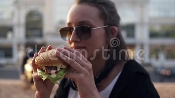 迷人的年轻女人兴高采烈地笑着双手拿着美味的汉堡吃穿着休闲装穿着视频的预览图