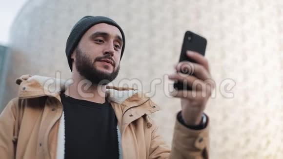 快乐的年轻胡须男有视频聊天拿着智能手机摄像头和朋友聊天外部视频的预览图