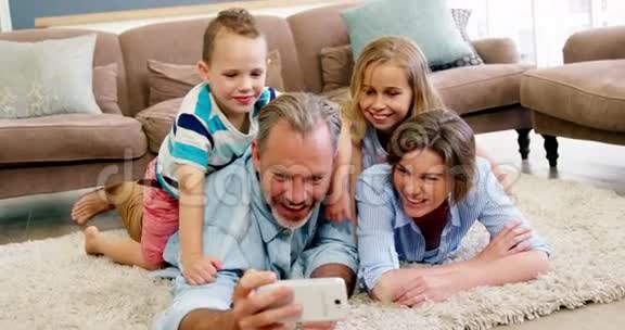 幸福的家庭躺在地毯上在手机上自拍视频的预览图