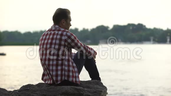 沮丧的成年男性坐在河边想着离婚孤独视频的预览图
