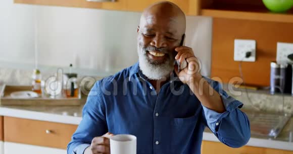 在厨房用手机说话时喝黑咖啡的老人视频的预览图
