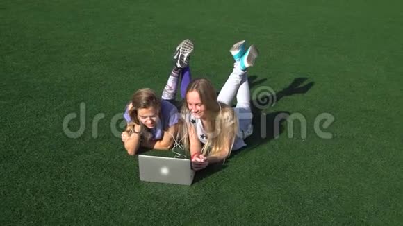 两个女孩用笔记本电脑躺在草地上视频的预览图