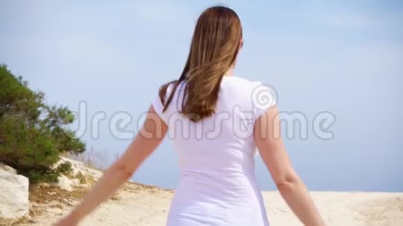 女人快乐地沿着沙路跳跃无忧无虑的女性举起手臂慢动作跳舞视频的预览图