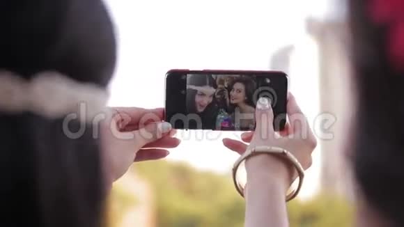 两个年轻女孩正在智能手机上拍照女性朋友在自拍时玩得很开心女人做着幸福的面孔视频的预览图