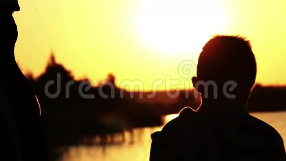 日落时分母亲抱着儿子在河边夕阳余晖映在水面上视频的预览图