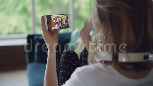 年轻女子在网上和朋友聊天用智能手机看着屏幕坐在沙发上说话视频的预览图