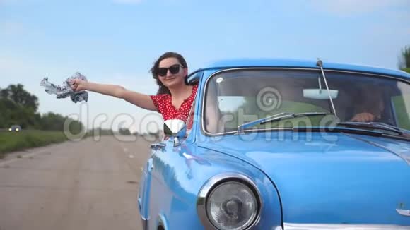 带着围巾的年轻女孩从老式汽车的车窗里探出来享受着乘车的乐趣女人从复古中脱颖而出视频的预览图