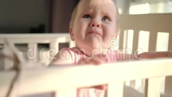 悲伤的婴儿在家的小床上哭泣蹒跚学步的孩子站在婴儿床上视频的预览图
