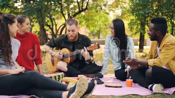 快乐的学生在秋天野餐时在公园里弹吉他和欣赏音乐的慢动作吉他手在演奏视频的预览图