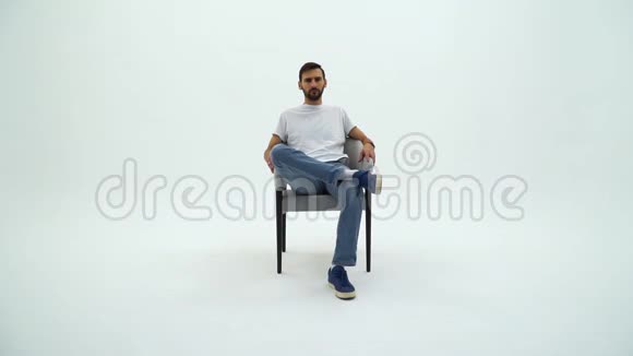 英俊的男人穿着白色的t恤和白色背景上的椅子人从椅子上站起来离开视频的预览图